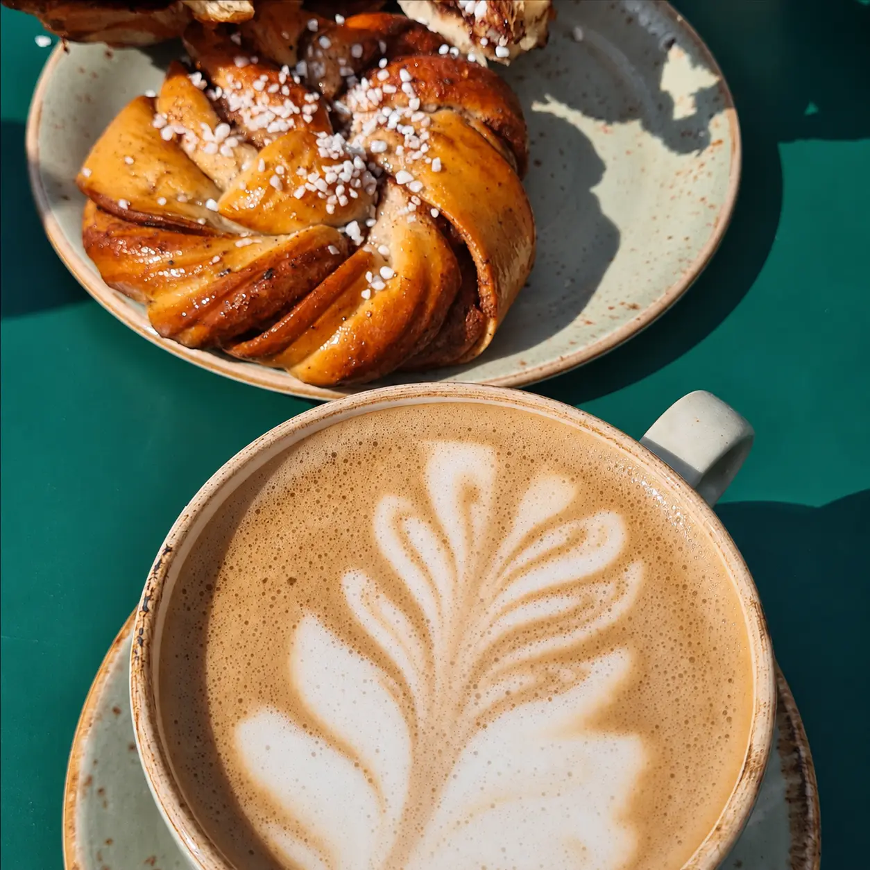 Zimtschnecke und Latte auf einem grünen Tisch